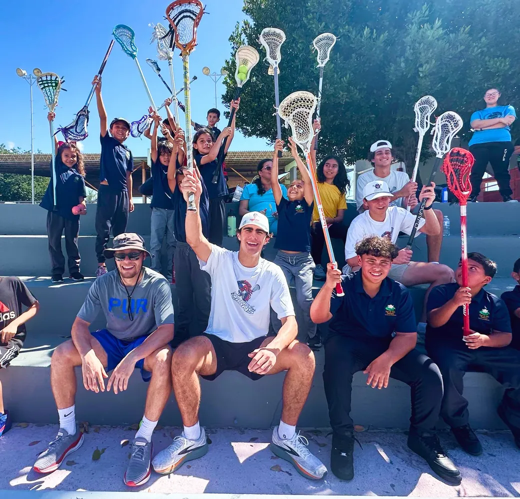 Youth clinic with players and kids raising lacrosse sticks